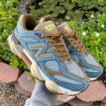 Blue and tan New Balance sneakers being held outdoors, showing the side logo and chunky sole.