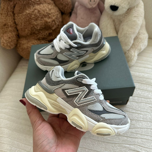 Gray New Balance sneakers with a chunky cream sole, held in front of a dark shoe box and plush bears in the background.