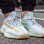Close-up of mint-green athletic sneakers with light blue laces on a person standing on a paved street.