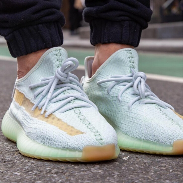 Close-up of mint-green athletic sneakers with light blue laces on a person standing on a paved street.