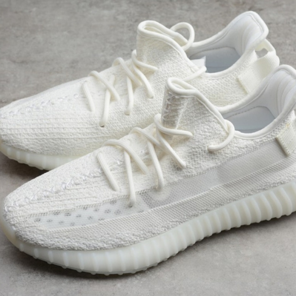 Pair of white knitted sneakers with chunky ribbed soles on a gray surface.