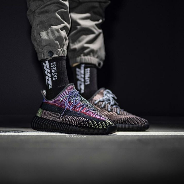 Colorful knit sneakers with a black chunky sole on dark background, worn with black socks and cargo pants.