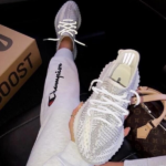 Person wearing white Champion sweatpants holds a pair of white knit sneakers, with a Boost box nearby.