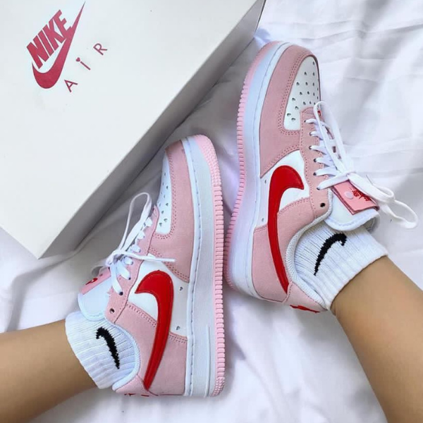 Pink and white Nike Air sneakers with red swoosh, worn on feet beside a Nike shoebox.