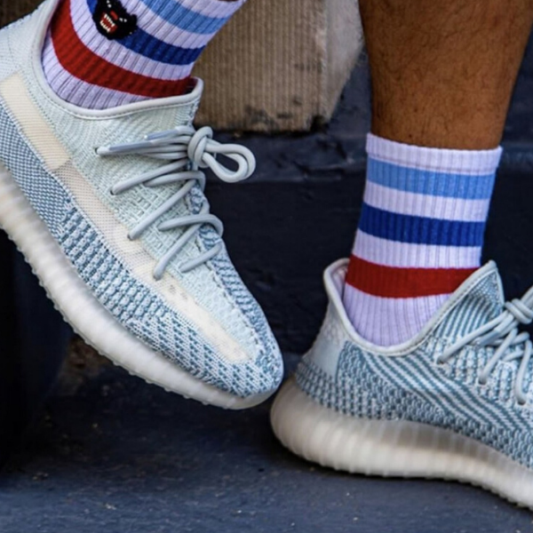 Light blue knit sneakers with pale laces on a dark stair, paired with red, white, and blue striped socks.