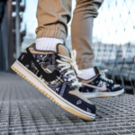 Close-up of navy blue patterned sneakers with white laces on a metal grate, beige pants, and white socks visible in the background while stepping forward.
