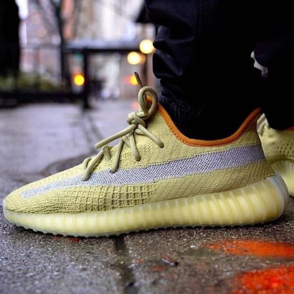 Close-up of a yellow knit sneaker with laces tied, resting on a wet city sidewalk edge.