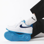 Side view of a white Nike sneaker with a bright blue sole and blue swoosh, worn with a white sock against a light background