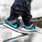 Person wearing black and white sneakers with teal swoosh stepping on a wet surface, reflecting in puddle.”,
