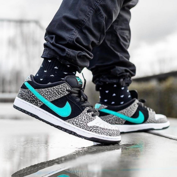 Untitleddesign_47_1295985a-6fb6-487e-bc6e-dd6b8f3c3684 Person wearing black and white sneakers with teal swoosh stepping on a wet surface, reflecting in puddle.”,