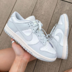Light blue Nike sneakers with white overlays being held by a hand against a wooden deck background.