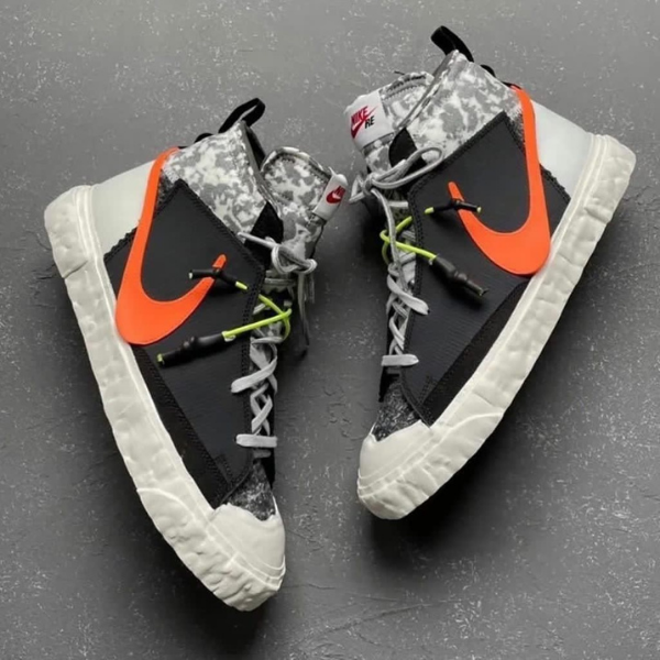 Pair of black and gray Nike high-top sneakers with bright orange Swoosh, laces tied, on a dark textured surface.