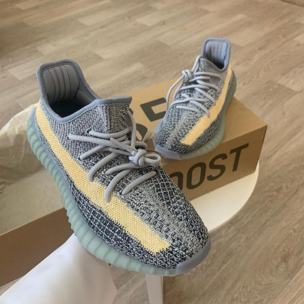 Gray knit sneakers with a pale yellow side stripe and light teal sole, resting on a BOOST box in a home setting.