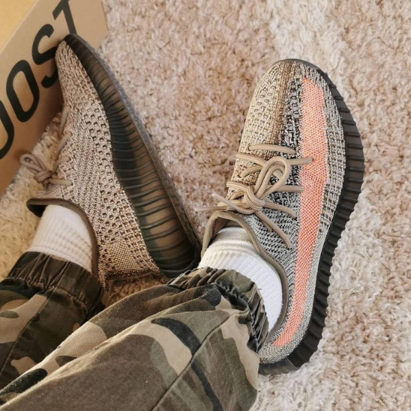 Person wearing beige and gray knit sneakers with white socks, camo pants, resting feet on a beige carpet.