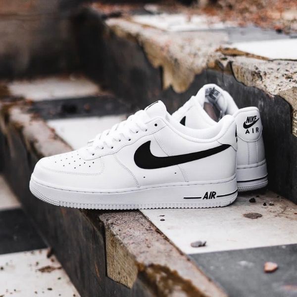 White Nike Air Force 1 sneakers with a black Swoosh resting on weathered concrete steps.