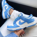 Blue and white Nike sneakers with a white swoosh, worn with white joggers and a denim jacket on a lap.