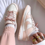 Pastel pink and white sneakers with laces on a person’s feet, wearing light pink pants