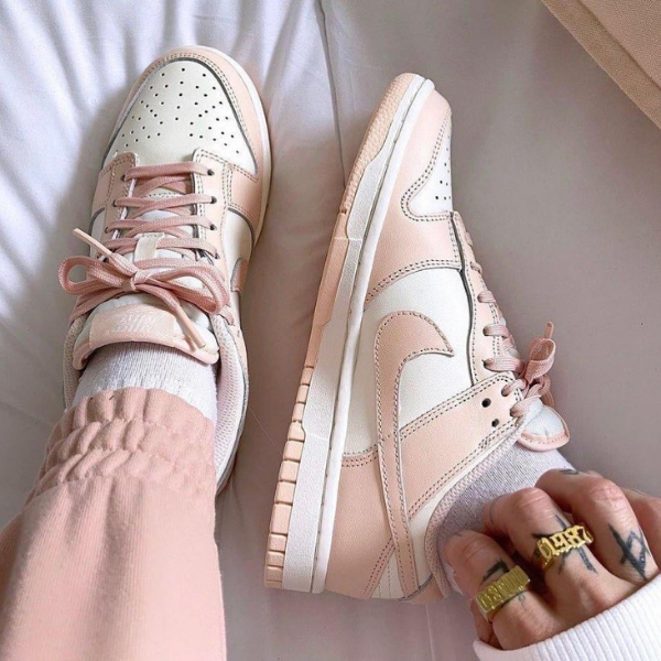 Pastel pink and white sneakers with laces on a person’s feet, wearing light pink pants