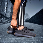 Person in black athletic shoes with striped track pants bending down to tie the laces on a paved path.
