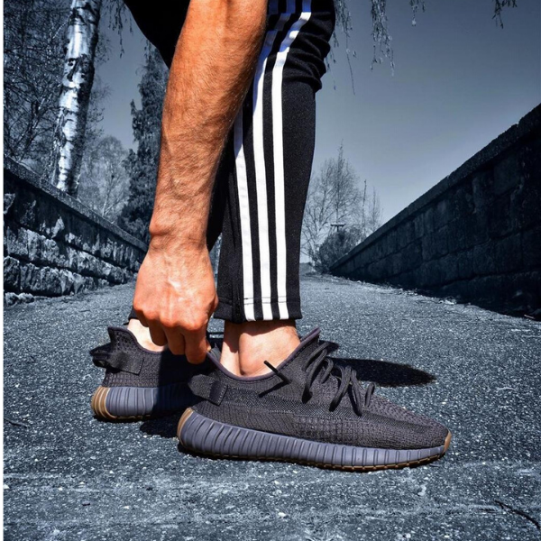 Person in black athletic shoes with striped track pants bending down to tie the laces on a paved path.