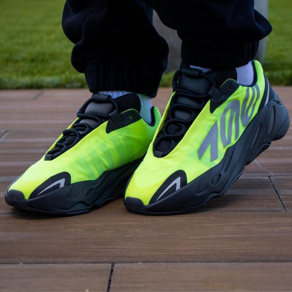 Pair of neon yellow-green athletic sneakers with black soles and laces resting on a wooden deck.