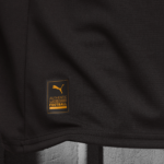 Close-up of black textured sports fabric with an orange Puma label that says 'AUTHENTIC LICENSED FOOTBALL'.