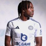 Portrait of a man with dreadlocks wearing a white Leicester City football jersey, looking to the right.