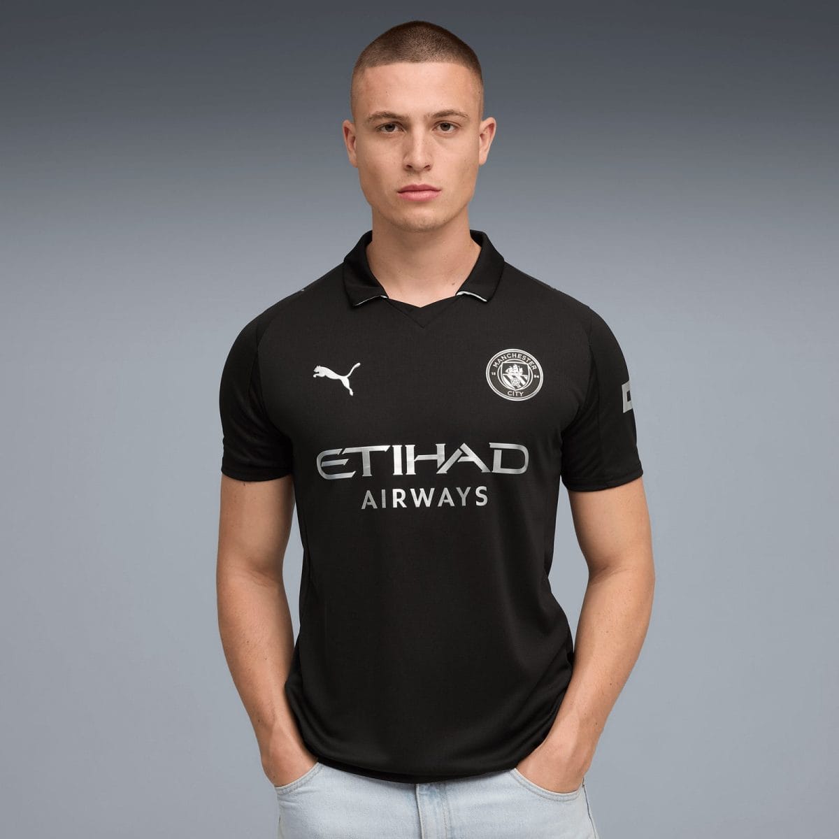 Man wearing a black Manchester City football jersey with Etihad Airways sponsor, standing against a gray gradient background.