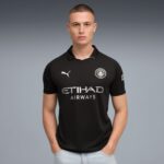 Man wearing a black Manchester City football jersey with Etihad Airways sponsor, standing against a gray gradient background.