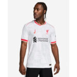 Male model wearing a white Liverpool FC jersey with red trim and the Standard Chartered sponsor logo.