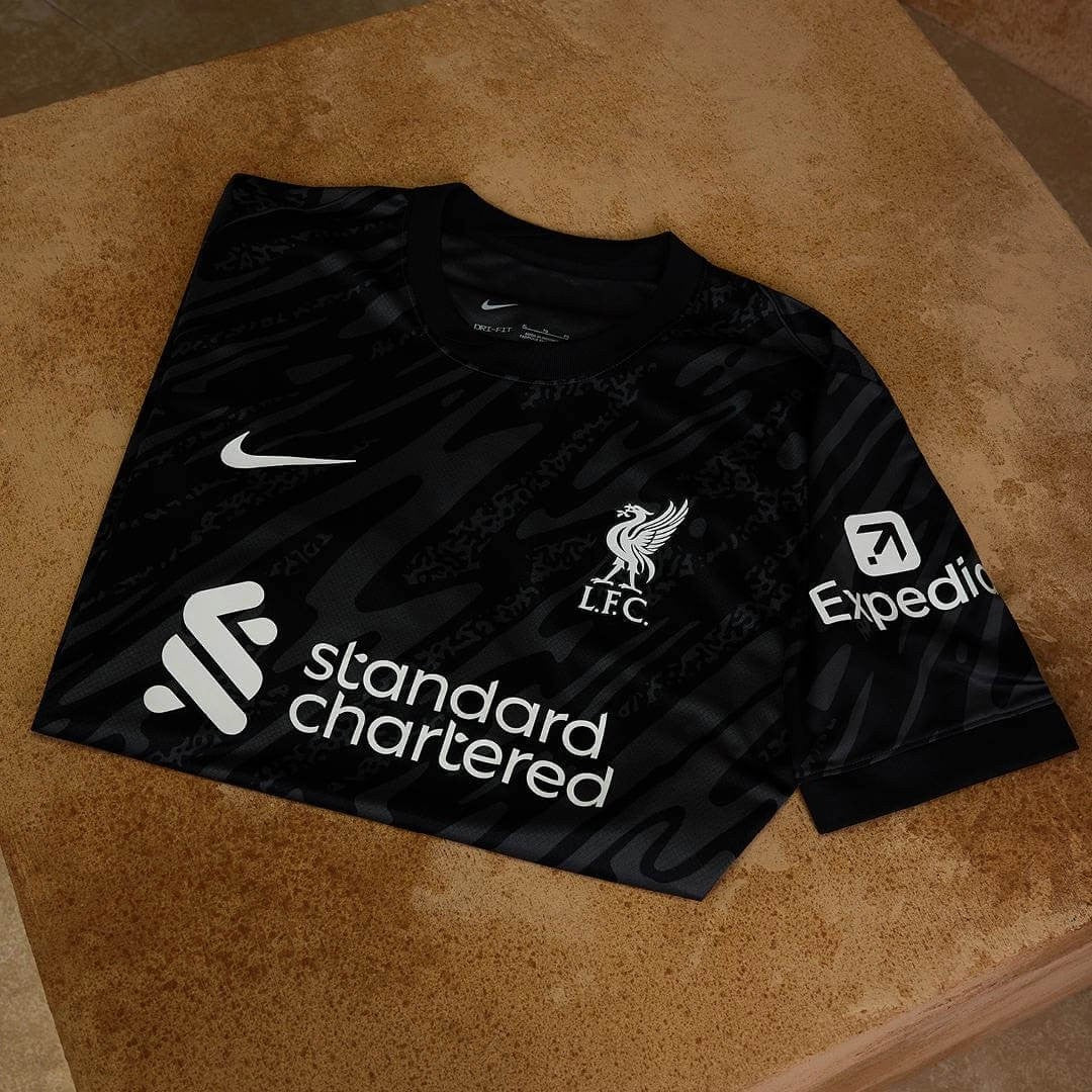 VHuMvLorK1pEHxZ_8da17590-f78c-463c-9951-87481409d9a8 | UAE SPORT STORE Black Liverpool FC football jersey laid flat on a tan surface, featuring the club crest and sponsor logos (Standard Chartered and Expedia) with a white Nike swoosh.