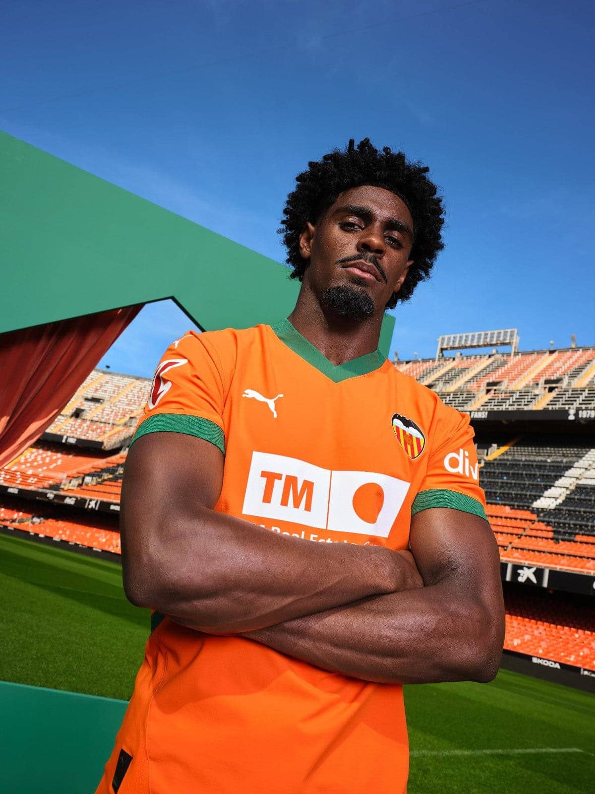 VIowSOw7hyH1P4O | UAE SPORT STORE Athlete wearing an orange Valencia FC jersey stands with arms crossed on a football pitch.