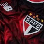 Close-up of a red-to-black SPFC soccer jersey showing the New Balance logo and the shield crest with five gold stars above it.