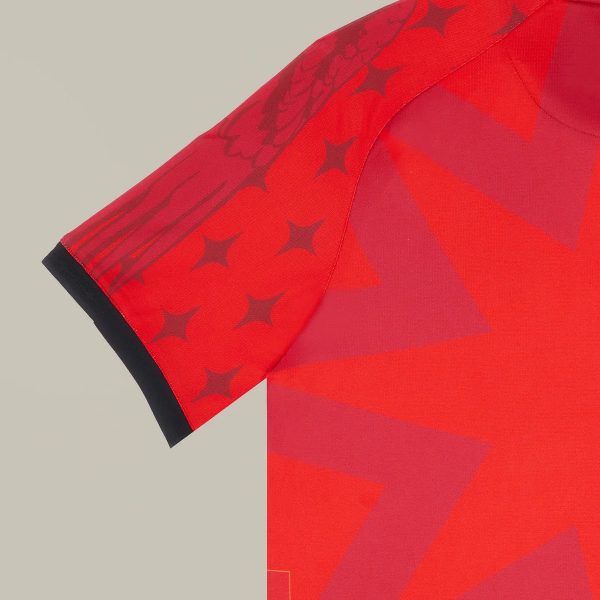 Close-up of a red athletic jersey sleeve with a black cuff and geometric star patterns on the fabric read as a design detail.