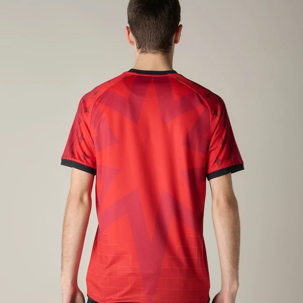 Back view of a person wearing a red geometric-patterned sports jersey with black cuffs and collar, standing against a neutral background.