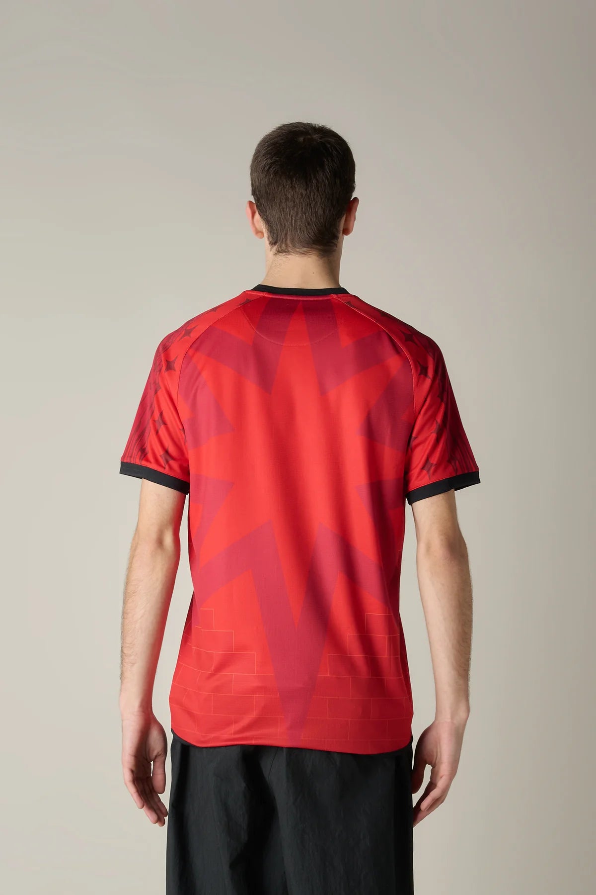 VeneziaFCindossato-48_crop | UAE SPORT STORE Back view of a person wearing a red geometric-patterned sports jersey with black cuffs and collar, standing against a neutral background.