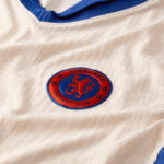 Chelsea Football Club crest on a white jersey with blue collar, close-up detail
