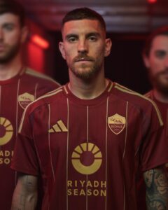 Close-up of a man in a maroon striped Roma football jersey, facing the camera.