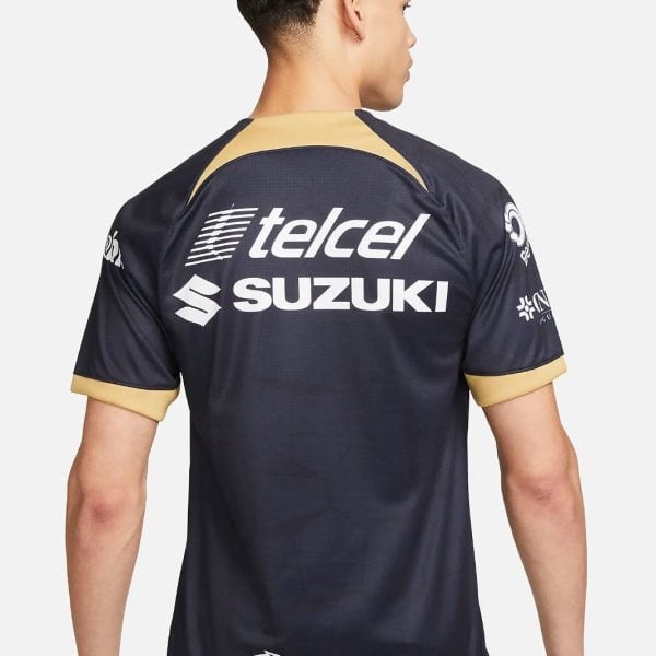 Back view of a man wearing a navy jersey with tan trim, showing Telcel, Suzuki, and Caliente.mx logos on the back.