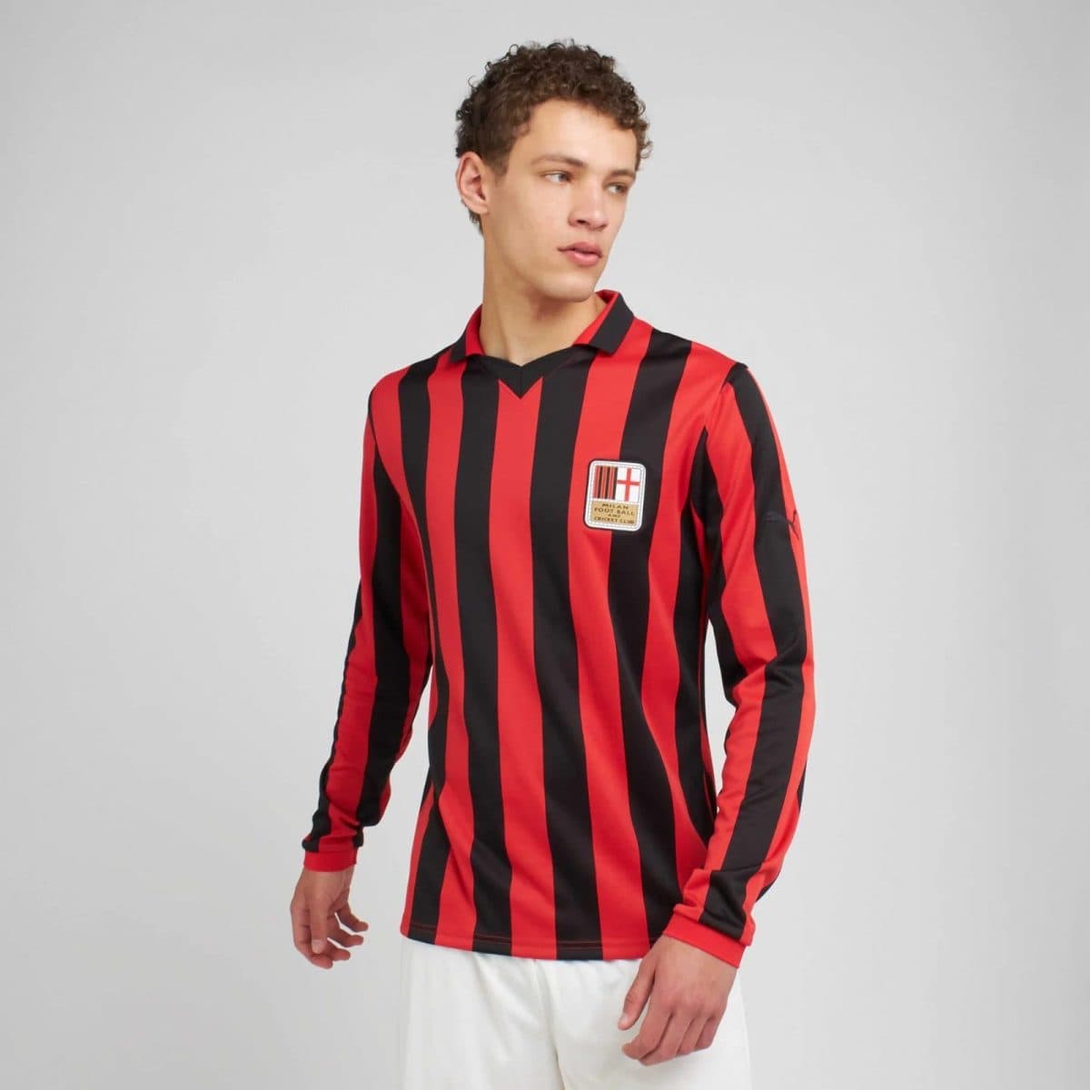 Person wearing a red and black vertical striped soccer jersey with a crest on the left chest, standing against a plain gray background.