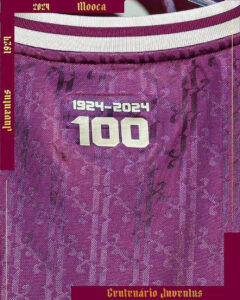 Close-up of a purple jersey with a large white '100' and the years '1924‑2024', commemorating the centennial of Juventus, with 'Centenário Juventus' text along the bottom.