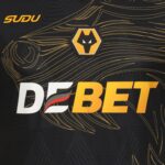 Close-up of a dark jersey with bold white and orange text reading 'DEBET' and a yellow-and-black wolf hex logo above it.