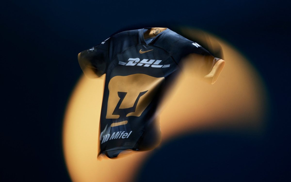 Dark blue sports jersey suspended mid-air with a large gold number 7 and DHL logo, set against a dark background with orange bokeh lights.