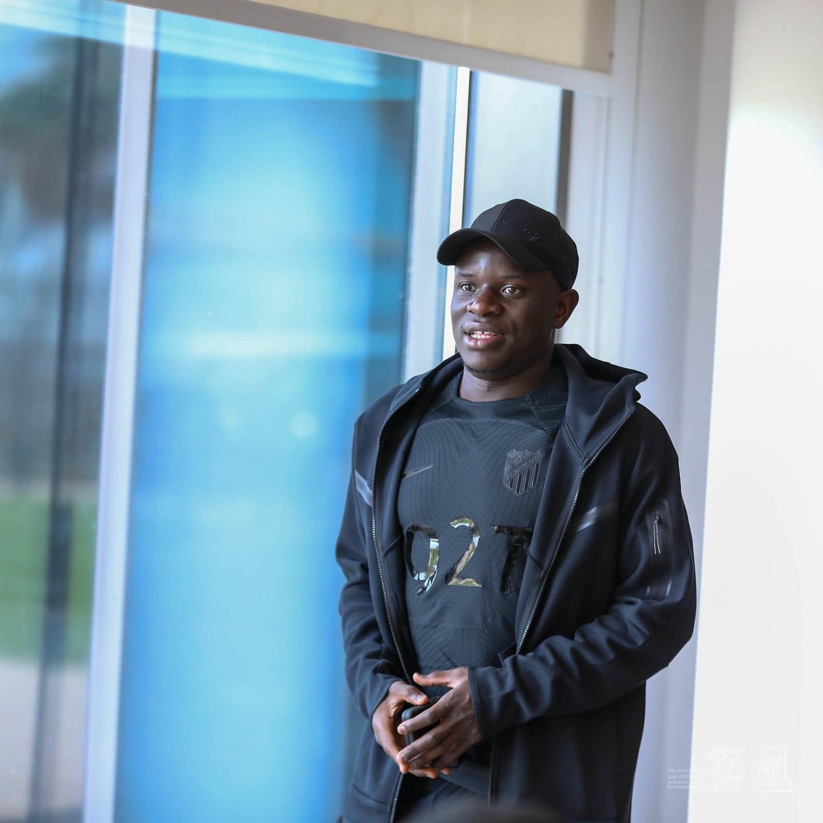 WXmHtO239iLdLQC | UAE SPORT STORE Man in a black cap and jacket stands by a large window, looking to the side.