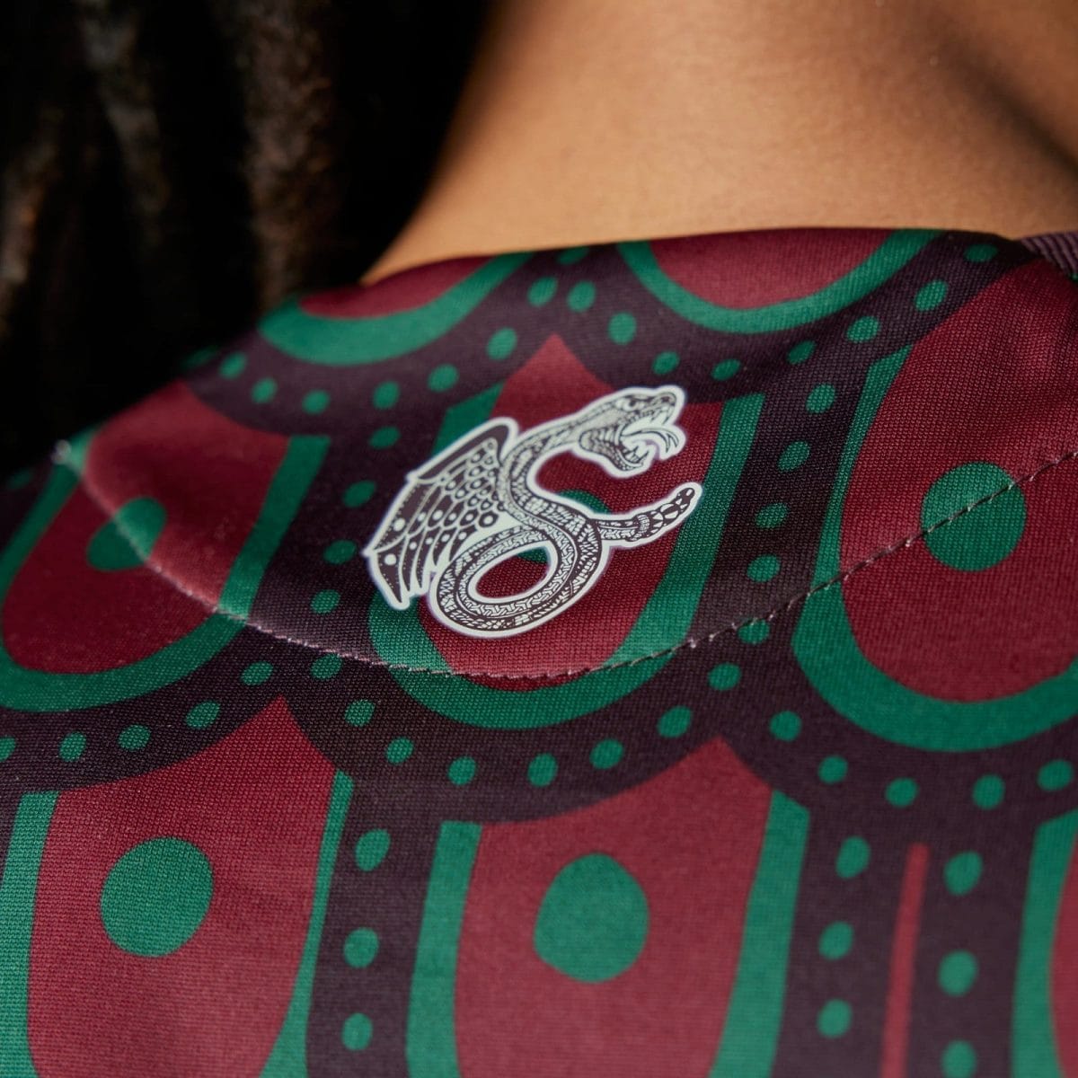 Close-up of patterned fabric (burgundy and green) with a white crocodile logo.