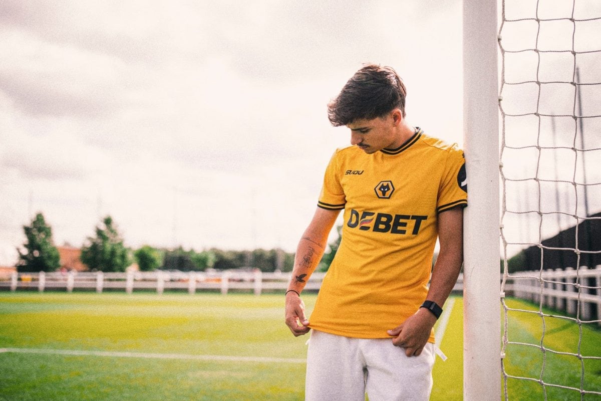 Young man in a yellow soccer jersey leaning against a goalpost on a green field.