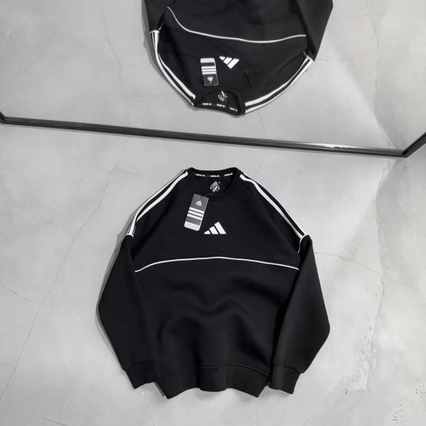 Two black Adidas track jackets with white piping and logo, laid flat on a light gray floor with tags attached.
