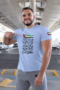 WhatsAppImage2020-11-24at7.53.52PM_1_7b9ebc11-cf67-40a2-97af-f3cb028c767a | UAE SPORT STORE Smiling man in a light blue T-shirt with Arabic calligraphy and a UAE flag on the sleeve, standing in a parking lot under an overpass.