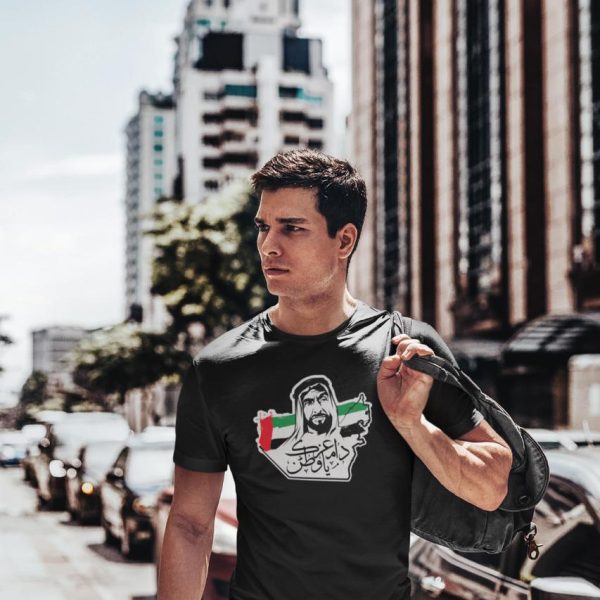 WhatsAppImage2020-11-24at7.53.53PM_8ecaeb5a-254a-4ac9-b70a-bc295ac1c8cc | UAE SPORT STORE Man walking down a city street wearing a black T-shirt with a Arabic-script graphic and carrying a backpack over his shoulder.