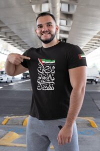 WhatsAppImage2020-11-24at7.53.58PM_1_75f46fbc-2e1f-4d65-ba74-2d8101e33871 | UAE SPORT STORE Smiling man in a black T‑shirt with Arabic typography, pointing to the print under a highway overpass.